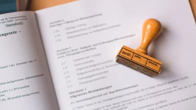 Aufgeschlagenes Gesetzbuch mit einem Holzstempel mit der Aufschrift geprüft