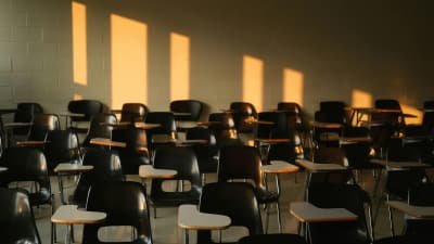 Leerer Seminarraum mit Reihen leerer Stühle, warmes Licht fällt durch die Fenster