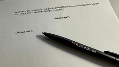 Gutachten zu einer Bachelorarbeit mit der Bewertung 1,0 sehr gut, daneben ein Kugelschreiber mit dem Aufdruck I love Hochschule Harz