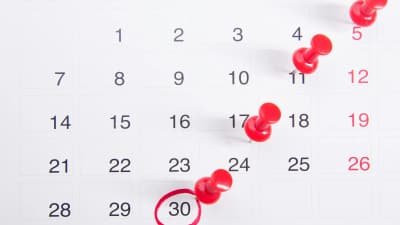 Kalender mit roten Pinnnadeln und einem rot umkreisten Datum als Symbol für eine nahende Frist