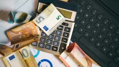 Taschenrechner mit mehreren Euro-Geldscheinen und Unterlagen auf einem Schreibtisch